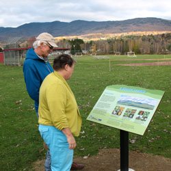 A man and a woman read a panel describing the culture and history of the Green Mountain Byway. 