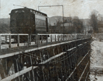 A black and white picture of an 1800s trolley on an elevated wooden track.