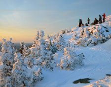 A group of hikers stand at the top of a mountain covered in snow watching the sunset. 