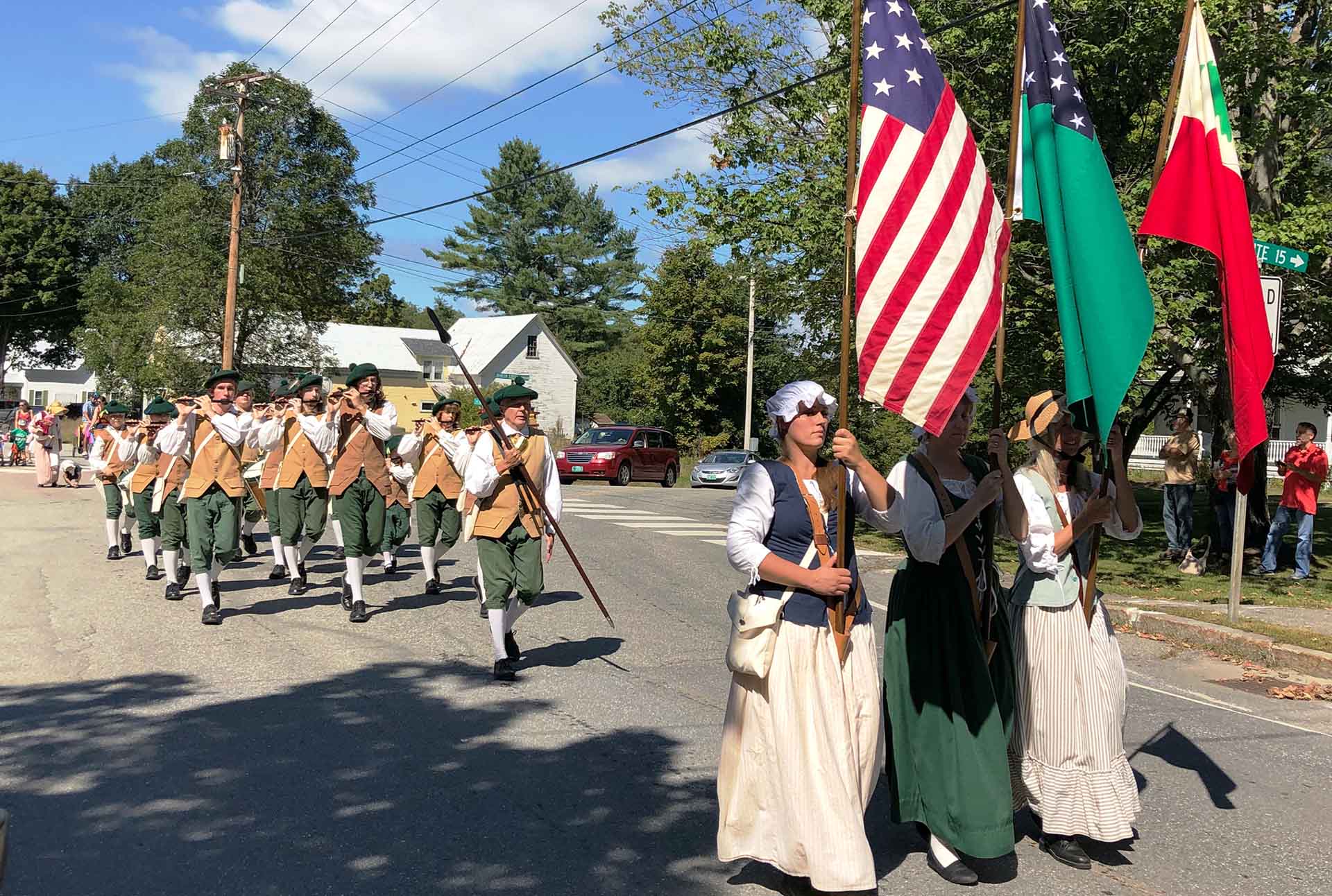 Women and men march in a parade dressed in period costumes. 