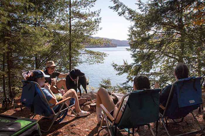 Two couples and a dog gather lakeside at a tent site on a large lake.