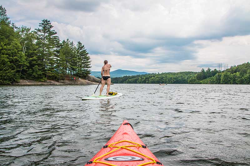 A woman paddleboards while the photographer takes a picture from their kayak behind her.