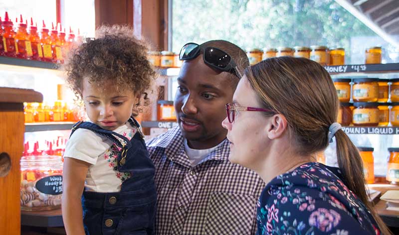 A young couple holds their daughter in a store filled with shelves of local honey.