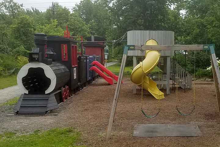 A children's playground with a climbing structure and and playset shaped like a train. 