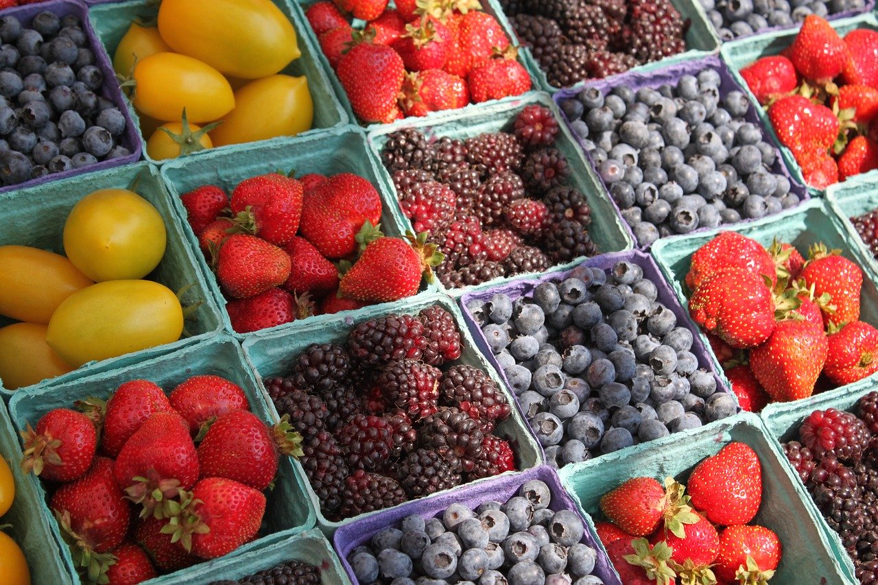 Baskets of strawberries, blackberries, blueberries, and yellow tomatoes make a colorful outdoor display.