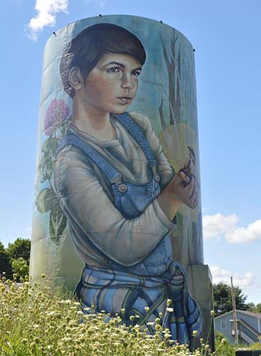 A mural depicting a boy in overalls, painted on the side of a silo. 